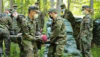 Ein Soldat auf einer Trage wird von mehreren Soldaten in Flecktarn im Wald getragen.