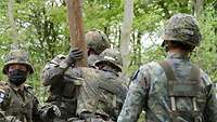 Vier Marinesoldaten in Flecktarn bei einer Ausbildung im Wald.