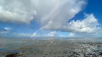 Eine Wolkenformation hat sich über dem Watt gebildet, am Horizont ist noch der Regenbogen zu erkennen. 