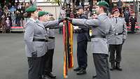 Mehrere Soldatinnen und Soldaten vor einer Flagge