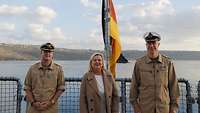 Die Wehrbeauftragte steht zwischen zwei Soldaten auf dem Flugdeck des EGV, hinter ihr weht die Deutschlandflagge