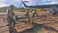 Belgische und norwegische Soldaten bringen einen Verwundeten auf einer Trage zum Rettungshubschrauber