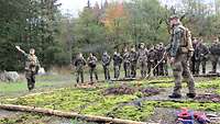 Zahlreiche Soldaten stehen um ein Geländemodell im Wald. Zwei Soldaten erklären daran das Gelände.