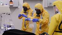 Three individuals in yellow protective gear are taking samples