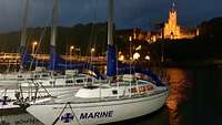 Festgemachte Segelboote bei Nacht. Im Hintergrund sieht die beleuchtete Marineschule Mürwik.