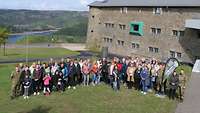 Eine Gruppe Menschen vor einem größeren Gebäude auf einer Wiese 