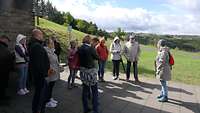 Eine Gruppe Menschen steht auf einer Terrasse neben einer Wiese. 