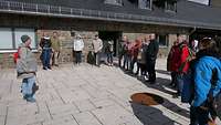 Eine Gruppe Menschen steht auf einer Terrasse und eine Frau redet zu der Gruppe. 