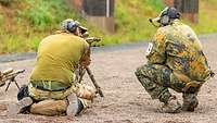 Auf einer Schießbahn kniet ein Soldat neben einem sitzenden Schützen mit einem Scharfschützengewehr.