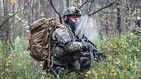 Ein Soldat kniet mit voller Montur im Wald und hält in der Hand ein G36. In der Umgebung ist es kalt, da er warme Luft ausatmet.