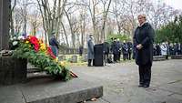 Ministerin Lambrecht steht vor einem Blumenkranz an einer Gedenkstätte auf einem Friedhof