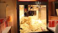 Eine beleuchtete Popcorn-Maschine befüllt mit frischem Popcorn. 