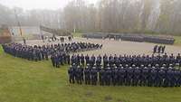 Hunderte Soldaten stehen in blauen Uniformen bei einem Ehrenmal. Es ist neblig.