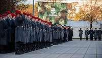 Soldaten sind auf einem Platz angetreten. Im Hintergrund eine Leinwand mit dem Logo der Bundeswehr. 