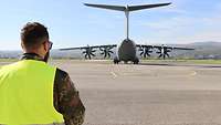 Auf einem Rollfeld steht ein Transportflugzeug. Im Vordergrund steht ein Soldat mit dem Blick zum Transportflugzeug.