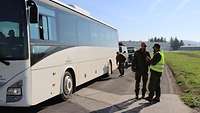 Zwei Soldaten unterhalten sich neben einem Bus. Dahinter kontrolliert ein Soldat die Reifen des Busses.