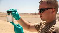 Ein Soldat hält ein Glas mit klarer Flüssigkeit in der Hand