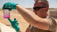 Soldat hält ein Glas mit teils pink gefärbter Flüssigkeit in der Hand