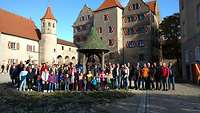 Eine Menschengruppe steht für ein Gruppenbild vor einer Burg.