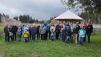 Menschengruppe auf einer Wiese, dahinter steht ein Pavillon. 