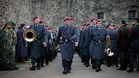 Soldaten mit Musikinstrumenten marschieren in drei Reihen hintereinander auf einen Platz ein.