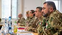 Soldaten verschiedener NATO- Staaten sitzen an einem Tisch und hören einem Vortrag zu