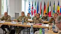 Soldaten verschiedener Nationen sitzen an Tischen und hören einem Vortrag zu.