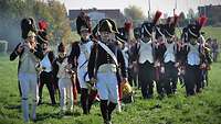 Männer in historischen Uniformen marschieren über eine Wiese. 