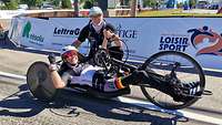 Ein Mann kniet neben einer glücklichen Sportlerin in ihrem Handbike