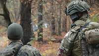 Zwei Soldaten stehen mit Flecktarnuniform in einem Waldstück
