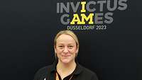 Eine Frau steht vor einer Werbung der Invictus Games 2023