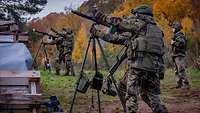 Soldaten schießen mit Maschinengewehren, die jeweils auf einem hohen Dreibein stehen.