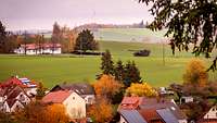 In der Ferne über der Silhouette einer Ortschaft fährt eine Haubitze auf einer kleinen Straße.