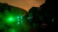 Bei Dunkelheit stehen Soldaten mit Taschenlampen neben ihren Fahrzeugen.