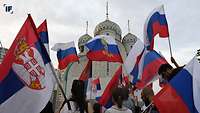 Russische und Serbische Flaggen werden vor einem serbischen Gebäude geschwenkt.