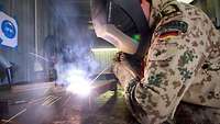 A soldier welds together metal parts in a camp workshop