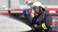 A Bundeswehr fireman wearing a respiratory mask holds a hose which has water coming out of it