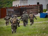 Mehrere Soldaten laufen mit Waffen in der Hand über eine Wiese auf ein Haus zu,