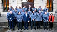 Viele Soldaten und drei Zivilisten stehen vor einer historischen Fassade in Formation.