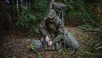 Ein Soldat kniet mit seiner Ausrüstung im Wald.