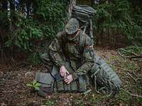 Ein Soldat kniet mit seiner Ausrüstung im Wald.