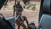 Zwei nigrische Soldaten nehmen während der Übung einen kampfunfähigen Gegner vor seinem Fahrzeug fest.