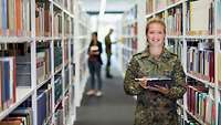 Eine Soldatin steht mit einem Tablet in der Hand in einer Bibliothek