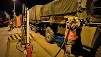 Mehrere militärische Fahrzeuge stehen an einer Tankstelle und ein Soldat betankt einen Lastkraftwagen.