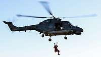 Ein Hubschrauber der Typ-Klasse "Sea Lynx" beim Flug. Aus dem Hubschrauber hat sich eine Person im Nikolaus-Kostüm abgeseilt.