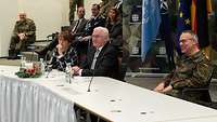 Bundespräsident, Gattin und Befehlshaber sitzen am Tisch in einem Konferenzraum. Im Hintergrund mehrere Soldaten