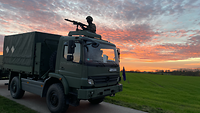 Bundeswehrfahrzeug in der Abenddämmerung. Ein Soldat mit Maschinengewehr ragt aus der Dachluke.