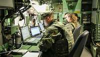 Mehrere Soldaten sitzen in einer Kabine vor Computern