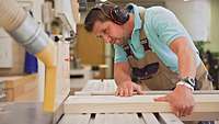 A carpenter of the Bundeswehr Service Centre cuts a wooden board with a bench saw