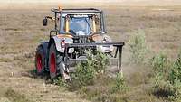 A man drives a tractor with a mulcher on a field at a major training area.